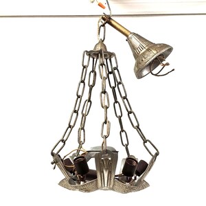 May include: A silver metal chandelier with five light bulbs and a chain hanging from the ceiling. The chandelier has a decorative design with a starburst pattern.