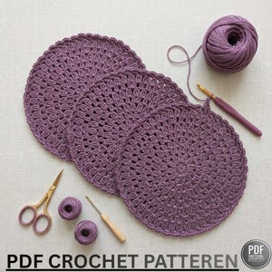 Puede incluir: Se muestran cuatro tapetes circulares morados de ganchillo con un borde festoneado. También hay un ovillo de hilo a juego, un ganchillo, una aguja lanera y unas tijeras pequeñas. El texto "PDF CROCHET PATTERN" está en la parte inferior de la imagen.