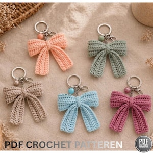 Peut inclure: Cinq porte-clés en forme de nœud papillon crochetés à la main, dans des tons pastel pêche, vert sauge, taupe, bleu clair et mauve. Chaque nœud est fixé à un porte-clés argenté avec une perle décorative. Le texte "PDF CROCHET PATTEREN" est en bas.