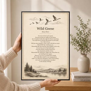 May include: A framed print featuring the poem Wild Geese by Mary Oliver. The text is centered above a landscape illustration of a river, trees, and mountains. At the top, a flock of geese flies across a cloudy sky. The background is cream-colored.