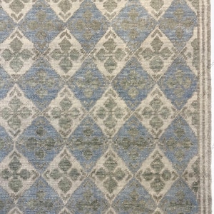May include: A close-up of a rug with a repeating diamond pattern. The diamonds are in shades of blue, cream, and gray, with a floral design in the center of each diamond. The rug has a textured appearance.