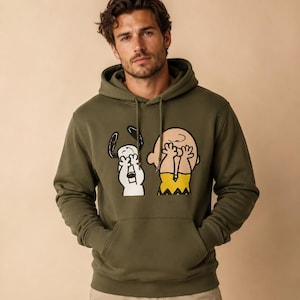May include: An olive green hooded sweatshirt featuring a graphic print of Snoopy and Charlie Brown covering their eyes with their hands. The hoodie includes a front kangaroo pocket, long sleeves, and matching drawstring cords at the neckline.