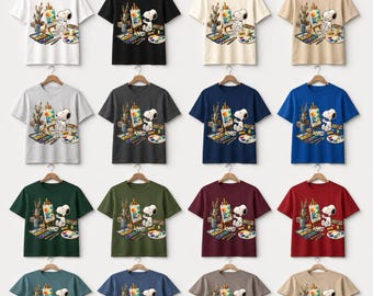 Könnte beinhalten: Eine Kollektion kurzärmeliger T-Shirts in verschiedenen Farben, jeweils mit einem Snoopy-Grafik als Künstler. Das Design umfasst eine Staffelei, eine Farbpalette und Pinsel. Die Shirts werden auf Kleiderbügeln präsentiert.