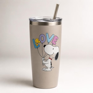 May include: A beige stainless steel tumbler with a clear lid and a metal straw. The tumbler features a graphic of Snoopy holding four balloons shaped like the letters L, O, V, and E, with Woodstock perched on the blue L balloon.