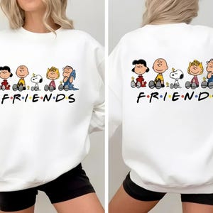 Puede incluir: Sudadera blanca con un diseño de dibujos animados de los personajes de Peanuts. La palabra "FRIENDS" está impresa en negro con puntos de colores. El diseño está en la parte delantera y trasera de la sudadera.