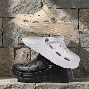 May include: A stack of three platform clogs in beige, white, and black. Each clog features a thick, textured sole, multiple ventilation holes across the upper, and a pivoting heel strap with a circular button detail labelled with the word SPORT.