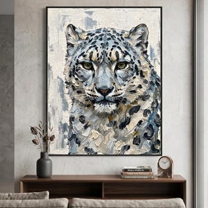 May include: A framed oil painting of a snow leopard. The artwork features a close-up of the animal's face, with green eyes and a coat of white, gray, and black spots. The painting has a textured, impasto style.