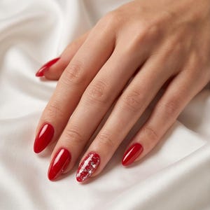 Könnte beinhalten: Mandelformige Fingernägel mit glänzendem, leuchtend rotem Nagellack. Der Ringfinger zeigt ein markantes Akzent-Nageldesign mit einer roten Grundfarbe, die mit unregelmäßigen, schimmernden silbernen Glitzerpartikeln auf der gesamten Nageloberfläche bedeckt ist.