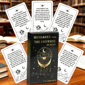 May include: A black oracle card deck titled "Messages From The Universe" with gold lettering and a crescent moon design. The deck includes 54 cards with inspirational messages and illustrations. Cards are scattered around the box.