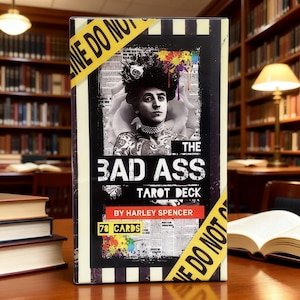 May include: A tarot deck box titled "THE BAD ASS TAROT DECK" by Harley Spencer. The box features a black and white image of a person with tattoos and a floral headpiece. The box is wrapped with yellow caution tape that reads "LINE DO NOT CROSS".