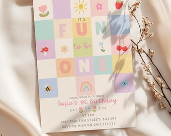 May include: A rectangular birthday invitation card featuring a pastel checkered grid with icons of a sun, flower, strawberry, mushroom, cherry, bee, rainbow, and butterfly. The text reads: IT'S FUN TO BE ONE, Sofia's 1st Birthday, SAT 15 JUN AT 1PM, 1234 TWO FUN STREET, SUBURB, RSVP TO MUM ON 0412 123 123.