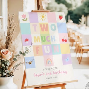 Op de afbeelding: Een rechthoekig verjaardagsbord op een houten ezel met een pastelkleurig ruitjespatroon en iconen van een tulp, zon, aardbei, paddenstoel, kersen, bij, regenboog en vlinder. De tekst luidt TWO MUCH FUN, WELCOME TO Sofia's 2nd Birthday, JUNE 15 20XX.
