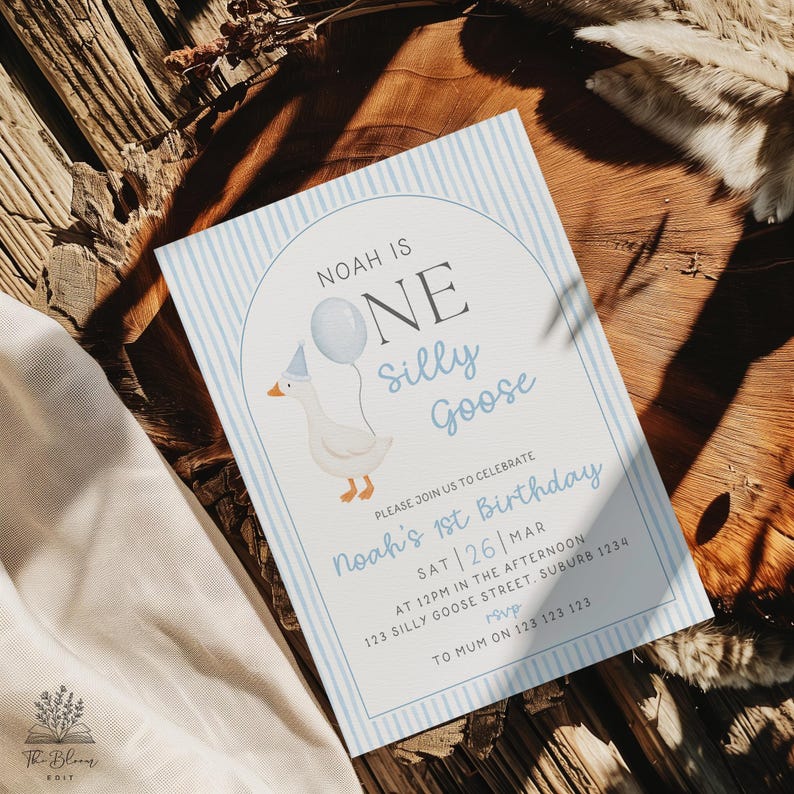 May include: A rectangular birthday invitation card with a light blue vertical striped border. The text reads: Noah is ONE silly goose. Please join us to celebrate Noah's 1st birthday. Sat 26 Mar at 12pm in the afternoon, 123 Silly Goose Street, Suburb 1234. RSVP to Mum on 123 123 123. A white goose wearing a party hat and holding a blue balloon is illustrated inside an arched frame.