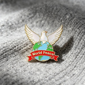 Puede incluir: Un broche de metal esmaltado en tono dorado que presenta una paloma blanca con las alas extendidas sobre un globo terráqueo con océanos azules y continentes verdes. Una cinta roja en la base muestra el texto World Peace en letras doradas.