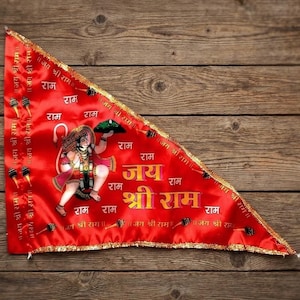 Può includere: Bandiera triangolare rossa con finiture dorate e testo in più lingue. La bandiera presenta un'illustrazione di una divinità e le parole "Jai Shri Ram" in giallo. La bandiera è esposta su uno sfondo di legno.