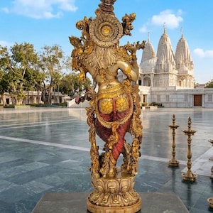 Puede incluir: Una estatua dorada detallada de una deidad, vista desde atr&aacute;s, se alza sobre una base de loto. La estatua presenta intrincadas tallas y est&aacute; adornada con detalles rojos y dorados. El fondo incluye un templo con agujas blancas y un cielo azul.