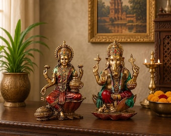 Puede incluir: Dos estatuas ornamentadas de las deidades Lakshmi y Ganesha, sentadas sobre pedestales de loto. Lakshmi viste un sari rojo y verde con joyas doradas y sostiene una vasija. Ganesha tiene un acabado dorado, collares de cuentas y ropas coloridas.