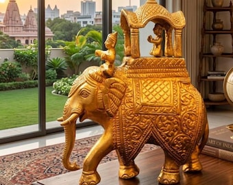 Puede incluir: Una figura decorativa dorada de un elefante con intrincados patrones en relieve. Una figura se sienta sobre el lomo del elefante bajo un dosel, mientras que otra pequeña figura está colocada dentro de la estructura. La pieza tiene un acabado.