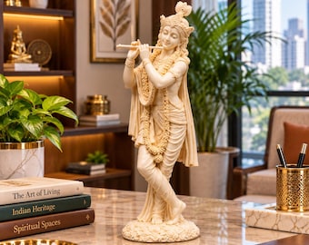 Puede incluir: Una estatua de resina de color crema de la deidad Krishna de pie en una pose de piernas cruzadas mientras toca una flauta. La figura lleva joyas ornamentadas, una prenda drapeada y una corona, con detalles tallados sobre una base circular.