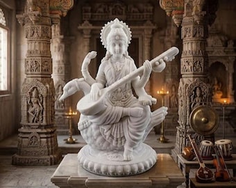 Puede incluir: Una estatua de mármol blanco de la deidad Saraswati sentada sobre una base de loto, con cuatro brazos y sosteniendo una veena. La figura está adornada con joyas tradicionales y una corona, colocada frente a una estructura arquitectónica de piedra tallada.