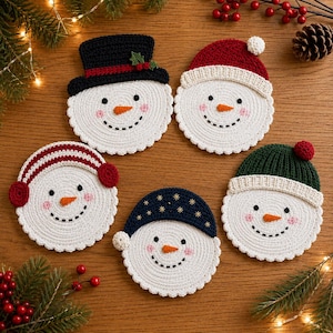 May include: Five round, white crocheted snowman coasters with embroidered faces, each wearing a different winter hat: a black top hat with holly, a red beanie, red earmuffs, a dark blue beanie with gold stars, and a dark green beanie.