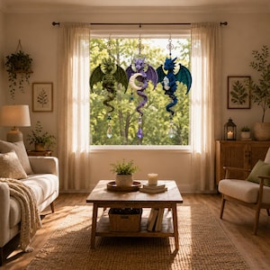 May include: Three hanging crochet dragon ornaments in green, purple, and blue, each featuring a coiled tail, textured wings, and a dangling crystal prism. The purple dragon holds a crescent moon, while the blue dragon holds a clear crystal.
