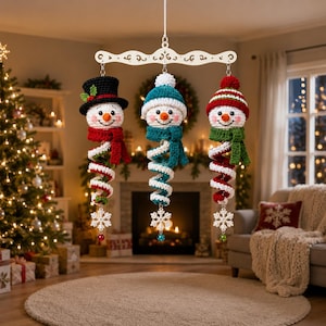 May include: A hanging mobile featuring three crocheted snowman figures suspended from a white decorative wooden bar. Each snowman has a unique hat, a colorful scarf, a spiral body, and a white snowflake ornament with a small bead at the base.