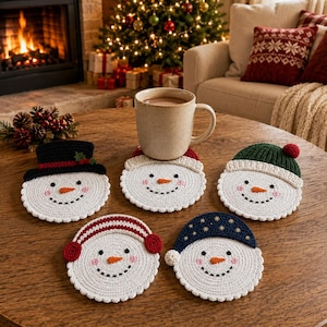 May include: Five round, white crocheted snowman coasters, each featuring a different colored hat: black with holly, cream, green with a pom-pom, red with earmuffs, and navy blue with gold stars. Each snowman has a carrot nose and rosy cheeks.
