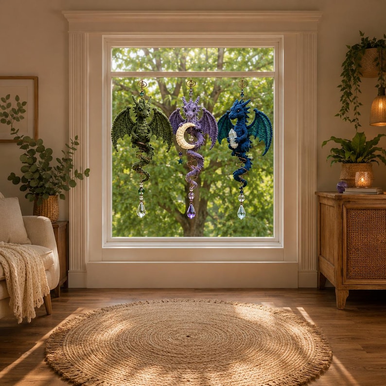 May include: Three crocheted dragon ornaments hanging in a window. The left dragon is green, the center is purple holding a crescent moon, and the right is blue holding a clear crystal. Each dragon features a dangling faceted crystal prism.