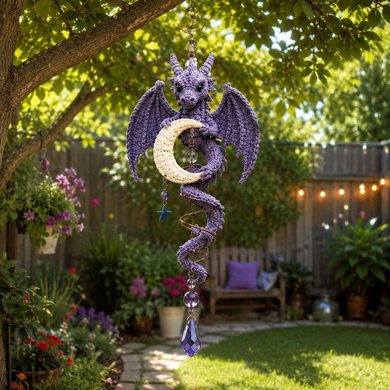 May include: A purple crocheted dragon hanging ornament featuring a cream-colored crescent moon held by the dragon, with a dangling blue star charm and a faceted purple crystal drop at the bottom, suspended by a metal chain with clear beads.