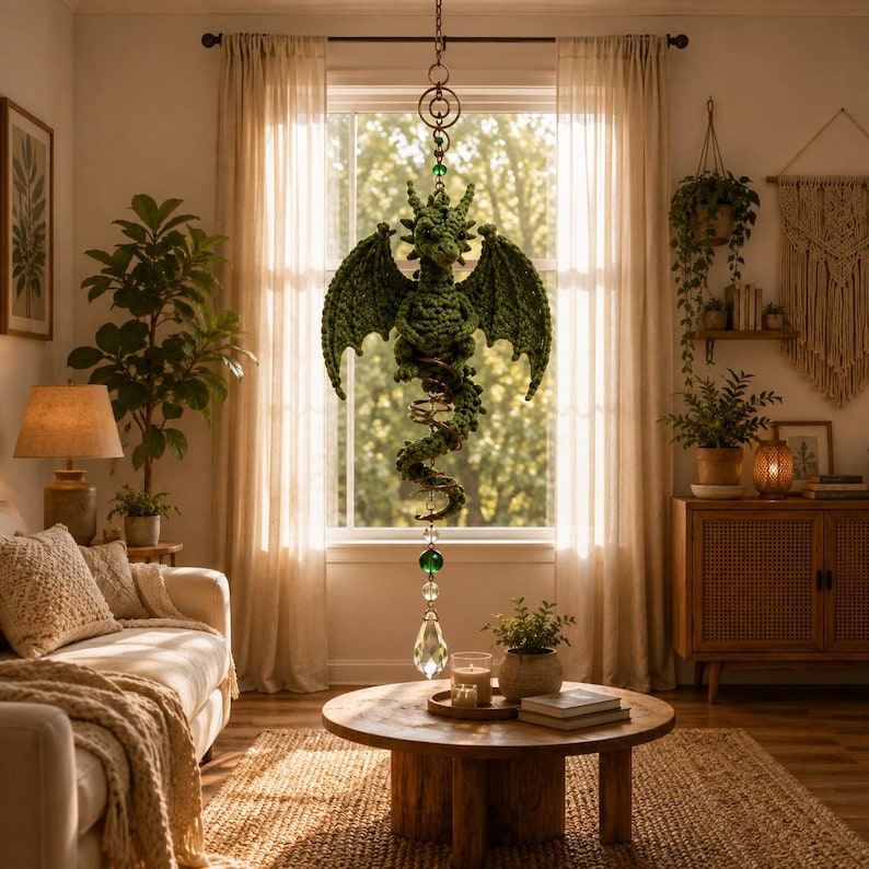 May include: A green crocheted dragon hanging ornament featuring a long, coiled tail and outstretched wings. The dragon is suspended from a metal chain with a clear crystal prism and a green glass bead dangling from the bottom of its tail.