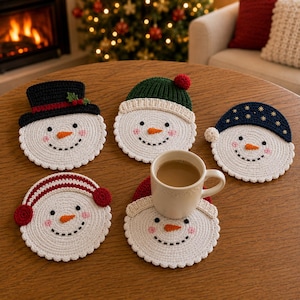 Pode incluir: Cinco porta-copos redondos de crochê branco em forma de boneco de neve, com rostos bordados, narizes de cenoura laranja e bochechas rosadas. Cada boneco usa um acessório de inverno diferente: cartola preta, gorro verde, azul, vermelho ou protetores de ouvido vermelhos.