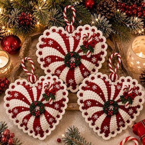 Può includere: Tre ornamenti all'uncinetto a forma di cuore con strisce rosse e bianche, ricami di fiocchi di neve bianchi e un bordo smerlato. Ogni ornamento è decorato con una piccola ghirlanda verde, bacche rosse e un bastoncino di zucchero in miniatura.