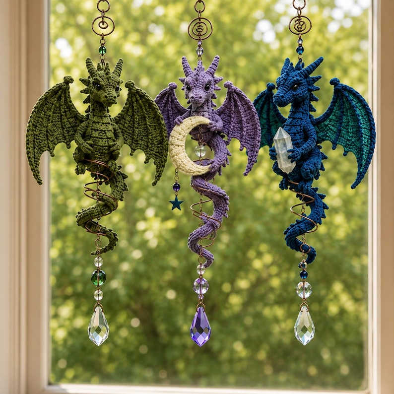 May include: Three hanging crochet dragon ornaments in green, purple, and blue. The purple dragon holds a crescent moon, while the blue dragon holds a clear crystal. Each dragon is suspended by a metal spiral and features a dangling crystal prism.