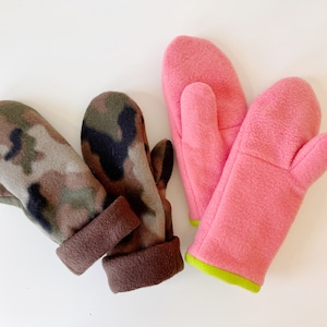 May include: Two pairs of fleece mittens. One pair is brown and green camouflage, the other is pink with a lime green trim.