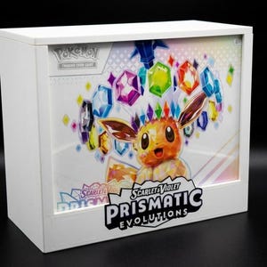 May include: A white box with a colourful illustration of an Eevee character and gemstones. The box is labelled "Pokemon Trading Card Game" and "Scarlet & Violet Prismatic Evolutions". The background is a mix of colours.