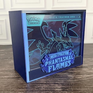 May include: A dark blue display case containing a Pokémon Trading Card Game Elite Trainer Box. The box features a blue outline of a Charizard and the text Mega Evolution Phantasmal Flames in a stylised blue flame-shaped font on the front.