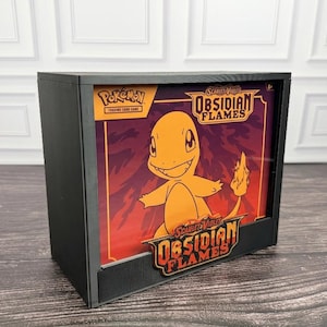 May include: A black rectangular display case featuring a Pokémon Trading Card Game Scarlet & Violet Obsidian Flames graphic. The insert shows a yellow Charmander character against a red and orange background with the Obsidian Flames logo.