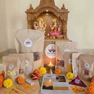 May include: A collection of brown paper pouches with clear windows, each featuring a PayToPlanet logo. The pouches are arranged before a wooden shrine containing Ganesha and Lakshmi statues, accompanied by marigold flowers and a lit brass lamp.