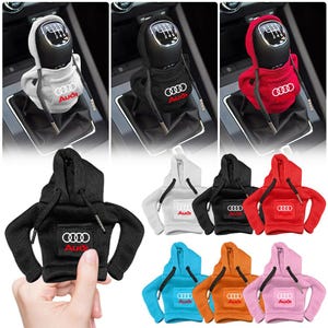 May include: A selection of car gear shift covers designed as miniature hoodies. The covers come in a range of colours, such as white, black, and red, each displaying the Audi logo. These hoodie-style covers are made to fit over the gear shift.