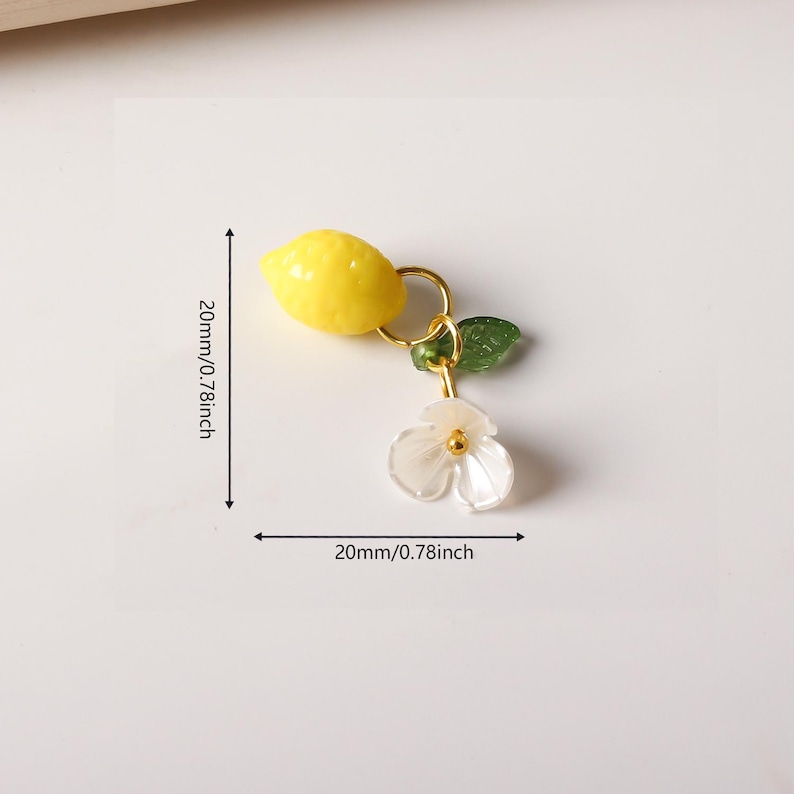 May include: A yellow lemon charm with a gold ring, a green leaf, and a white flower with a gold center. The charm is approximately 0.78 inches in length and width.
