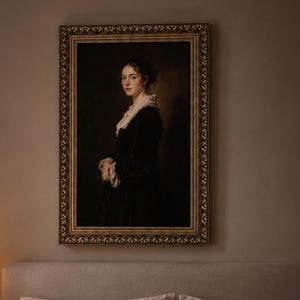 Op de afbeelding: Een ingelijst portretschilderij van een persoon in een donker kledingstuk met lange mouwen en een witte kanten kraag, in een sierlijke gouden lijst. Het kunstwerk hangt aan een neutraal gekleurde muur boven een bed met beige beddengoed.