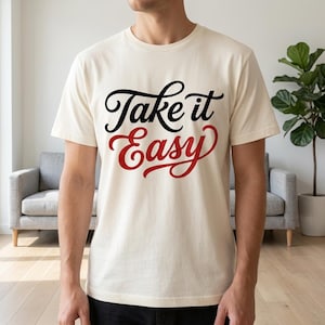 May include: Cream-colored t-shirt with the phrase "Take it Easy" in black and red script. The shirt is made of a soft material and is suitable for casual wear. The text is centered on the front of the shirt.