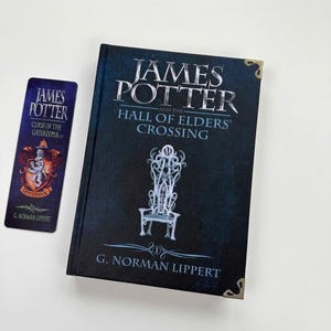 May include: A hardcover book titled James Potter and the Hall of Elders' Crossing by G. Norman Lippert with a dark blue cover featuring a white ornate chair illustration and metal corner protectors, accompanied by a matching rectangular bookmark.