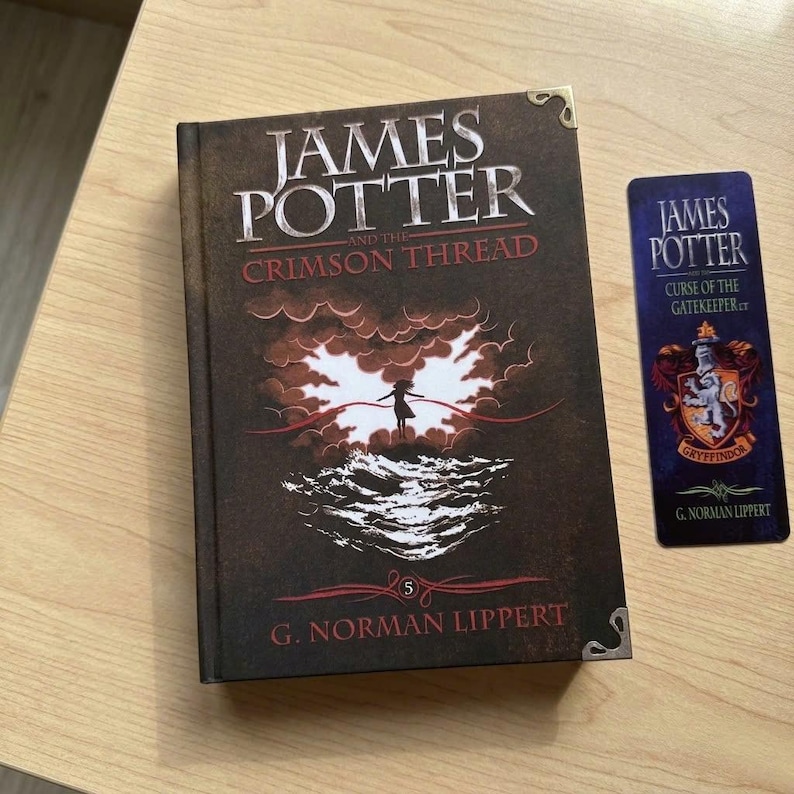 May include: A hardcover book titled James Potter and the Crimson Thread by G. Norman Lippert with a dark brown cover featuring a silhouette figure, clouds, and waves, alongside a matching rectangular bookmark with a crest and text.