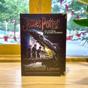 May include: A hardcover book titled James Potter and the Hall of Elders Crossing by G. Norman Lippert. The dark cover features an illustration of three figures standing before a large, glowing, toothy creature under a full moon in a forest.