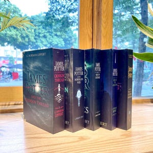 May include: A collection of five James Potter book series novels by G. Norman Lippert, including James Potter and the Crimson Thread, The Morrigan Web, Vault of Destinies, Curse of the Gatekeeper, and The Hall of Elders Crossing, standing upright.