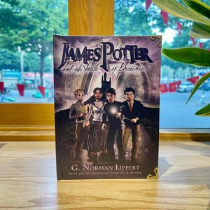 May include: A hardcover book titled James Potter and the Vault of Destinies by G. Norman Lippert. The cover features a purple and black illustration of four young characters standing before a dark castle, with one character holding a glowing light.