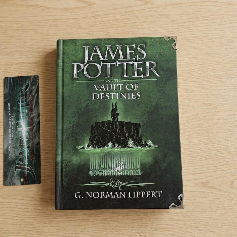 May include: A hardcover book titled James Potter and the Vault of Destinies by G. Norman Lippert with a dark green cover featuring a black silhouette of a castle on a cliff, accompanied by a matching vertical bookmark with the same book title.