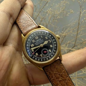 Puede incluir: Reloj Oris vintage dorado con esfera negra, n&uacute;meros y agujas blancos. El reloj tiene una correa de cuero marr&oacute;n. La esfera del reloj incluye el texto "ORIS WATERPROOF ANTI-SHOCK".